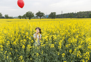 Porträt eines Jungen, der in einem gelben Blumenfeld steht und einen roten Luftballon hält - CUF20457