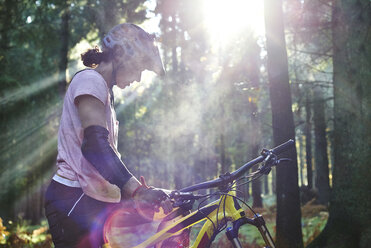 Mountainbikerin steht mit gesenktem Kopf im Sonnenstrahl, Forest of Dean, Bristol, UK - CUF20466