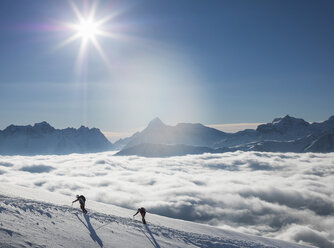 Zwei Bergsteiger an einem verschneiten Hang über einem Nebelmeer in einem Alpental, Alpen, Kanton Wallis, Schweiz - CUF20468