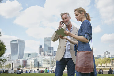 Mature man and woman outdoors, looking at digital tablet, man using smartphone - CUF20567