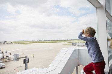Boy looking out of airport window at runway - CUF20573
