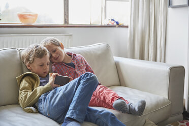 Jungen sitzen auf dem Sofa und schauen auf ihr Smartphone - CUF20575