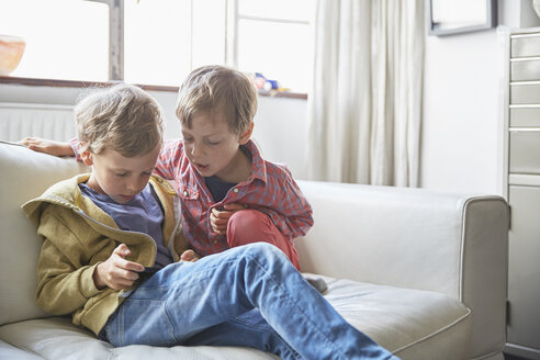 Jungen sitzen auf dem Sofa und schauen auf ihr Smartphone - CUF20576