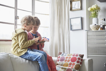 Jungen sitzen auf dem Sofa und schauen auf ihr Smartphone - CUF20605