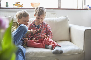 Jungen sitzen auf dem Sofa und schauen auf ihr Smartphone - CUF20606