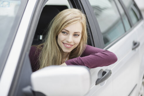 Langhaarige blonde junge Frau lehnt sich aus dem Autofenster in der Stadt - CUF20611