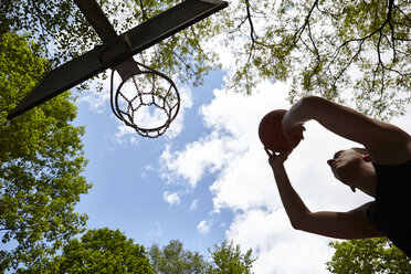 Low angle view of silhouetted young man aiming ball at basketball hoop - CUF20673