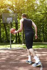 Rear view of young male basketball player running with ball on court - CUF20674