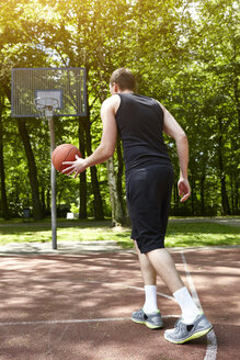 Rückansicht eines jungen männlichen Basketballspielers, der mit dem Ball auf dem Platz läuft - CUF20674