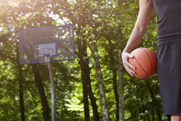 Ausschnitt eines jungen männlichen Basketballspielers, der einen Ball vor einem Basketballkorb hält - CUF20675