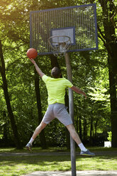 Rear view of young male basketball player jumping and throwing ball at basketball hoop - CUF20677