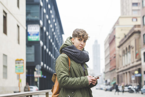 Young woman standing in street, holding smartphone - CUF20720