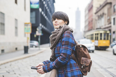 Young woman leaning on railing, holding smartphone - CUF20724