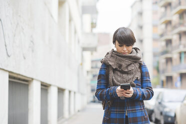 Junge Frau geht die Straße entlang und benutzt ihr Smartphone - CUF20741