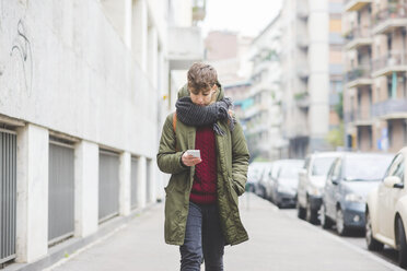 Young woman walking along street, using smartphone - CUF20742