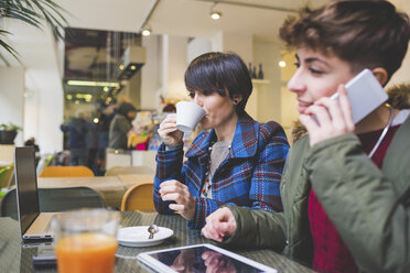 Zwei Schwestern im Café mit Laptop, digitalem Tablet und Smartphone - CUF20750