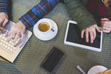 Zwei Frauen in einem Café, die einen Laptop und ein digitales Tablet benutzen, daneben Kaffee, Draufsicht - CUF20751