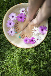 Young woman's feet in bowl of flower water on lawn - CUF20822