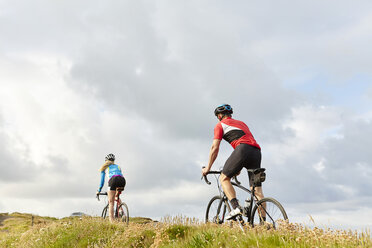 Cyclists riding past meadow - CUF20875