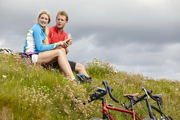 Cyclists relaxing and chatting on grassy hilltop - CUF20882