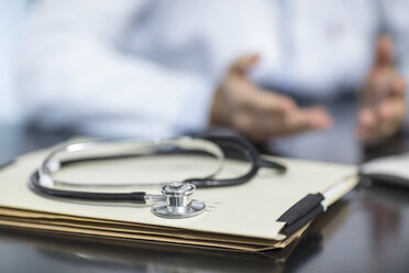 Akten und Stethoskop auf einem Schreibtisch in einer Arztpraxis mit einem Arzt im Hintergrund - ZEF15505