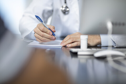 Arzt sitzt an seinem Schreibtisch und macht Notizen, lizenzfreies Stockfoto