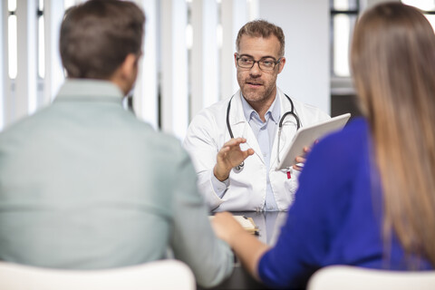 Arzt im Gespräch mit einem Paar in einer Arztpraxis, lizenzfreies Stockfoto