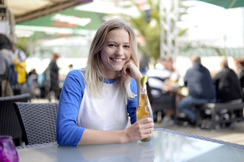 Blonde junge Frau mit Bierflasche im Biergarten, lizenzfreies Stockfoto