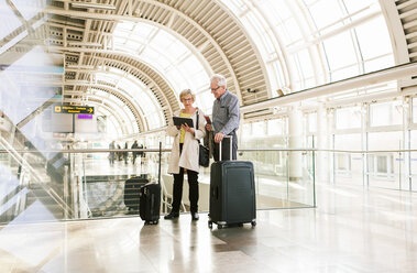 Full length of senior woman holding digital tablet by man standing with luggage at subway station - MASF07609