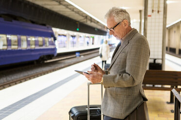 Seitenansicht eines älteren männlichen Pendlers, der ein Smartphone benutzt, während er in einer U-Bahn-Station steht - MASF07615