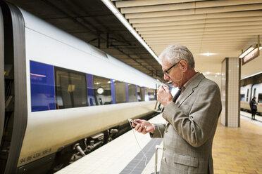 Seitenansicht eines älteren Mannes, der in einer U-Bahn-Station mit seinem Smartphone telefoniert - MASF07619