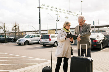 Älteres Paar, das ein digitales Tablet benutzt, während es mit Gepäck auf einem Parkplatz gegen den Himmel steht - MASF07622