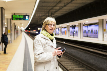 Ältere Frau schaut weg, während sie mit ihrem Smartphone in der U-Bahn-Station steht - MASF07623