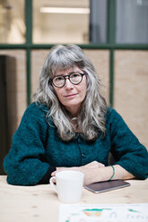 Portrait of confident smiling mature businesswoman having coffee at table in office - MASF07627