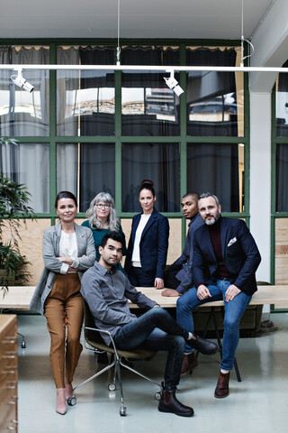 Porträt eines selbstbewussten Teams am Tisch in einem kreativen Büro in voller Länge, lizenzfreies Stockfoto