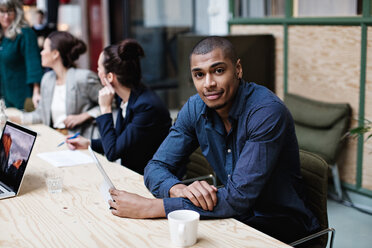 Portrait of young businessman sitting with female colleagues at table in office meeting - MASF07633