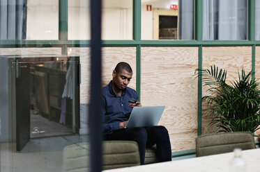 Geschäftsmann, der mit seinem Laptop online einkauft, während er im Kreativbüro sitzt - MASF07655