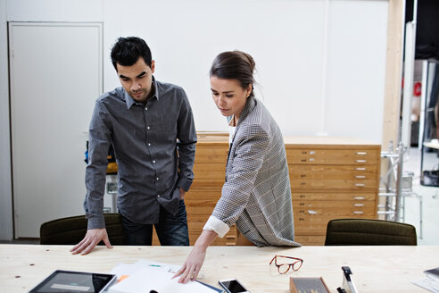 Confident male and female business colleagues discussing over documents at table in office - MASF07663