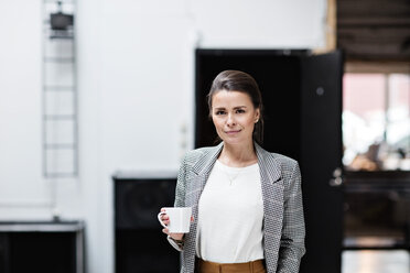 Portrait of beautiful smiling businesswoman having coffee while standing at office - MASF07666