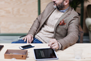 Midsection of businessman with digital tablet and smart phone sitting at table in creative office - MASF07675