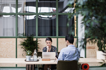 Professional using laptop while sitting with colleague at table in office - MASF07691