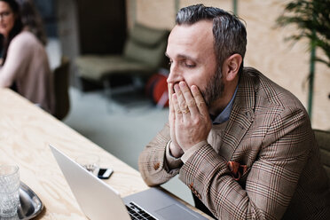 Tired businessman looking at laptop while sitting in office - MASF07698