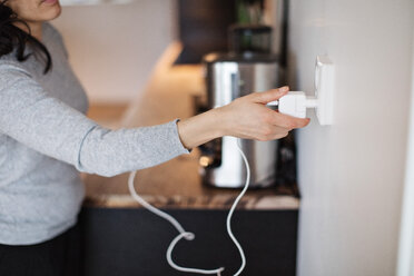 Midsection of woman plugging mobile phone charger on wall at home - MASF07713