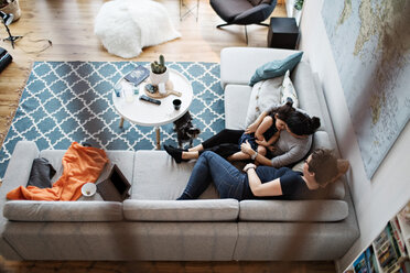 High angle view of lesbian couple talking with daughter while sitting on sofa by dog in living room at home - MASF07715
