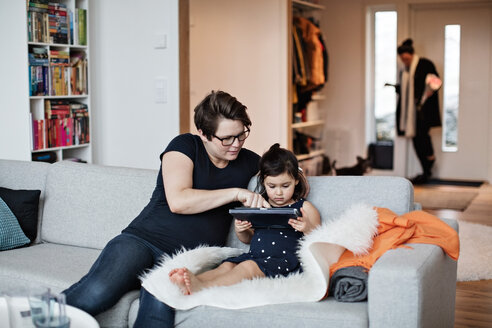 Mutter zeigt ihrer Tochter ein digitales Tablet, während sie zu Hause auf dem Sofa sitzt - MASF07732