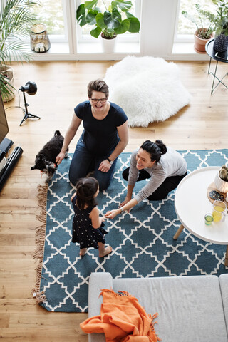 Mütter, die mit ihrer Tochter spielen, während sie im Wohnzimmer bei ihrem Hund sitzen, lizenzfreies Stockfoto