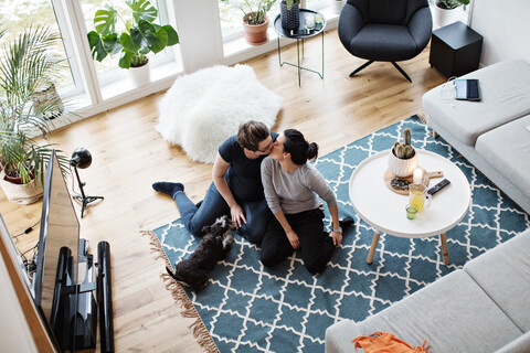 Hohe Winkel Ansicht der lesbischen Paar küssen, während sie von Hund auf Teppich im Wohnzimmer sitzen, lizenzfreies Stockfoto
