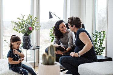 Lesbisches Paar, das sich unterhält, während das Mädchen über das Mobiltelefon im Wohnzimmer Musik hört - MASF07744