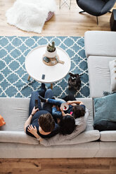 Directly above shot of lesbian couple sitting with daughter on sofa by dog in living room at home - MASF07750