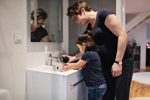Frau, die ihrer Tochter beim Händewaschen am Waschbecken im Haus hilft, lizenzfreies Stockfoto